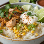 Chicken Street Corn Rice Bowls 4 A vibrant chicken street corn rice bowls topped with roasted corn, creamy sauce, fresh cilantro, and lime wedges, served on a wooden table.