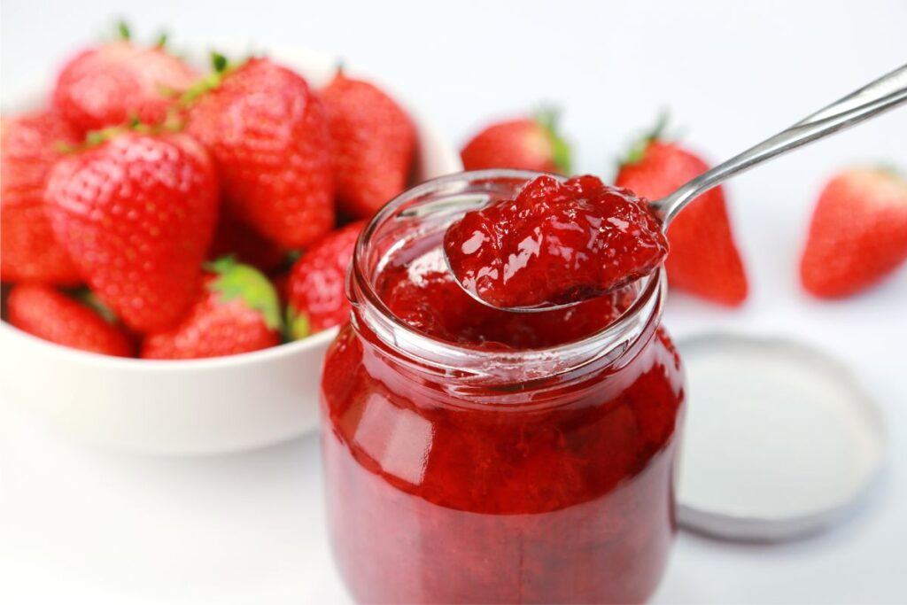 A cake slice with layers of moist vanilla sponge filled with strawberry jam and topped with a glossy strawberry jam glaze